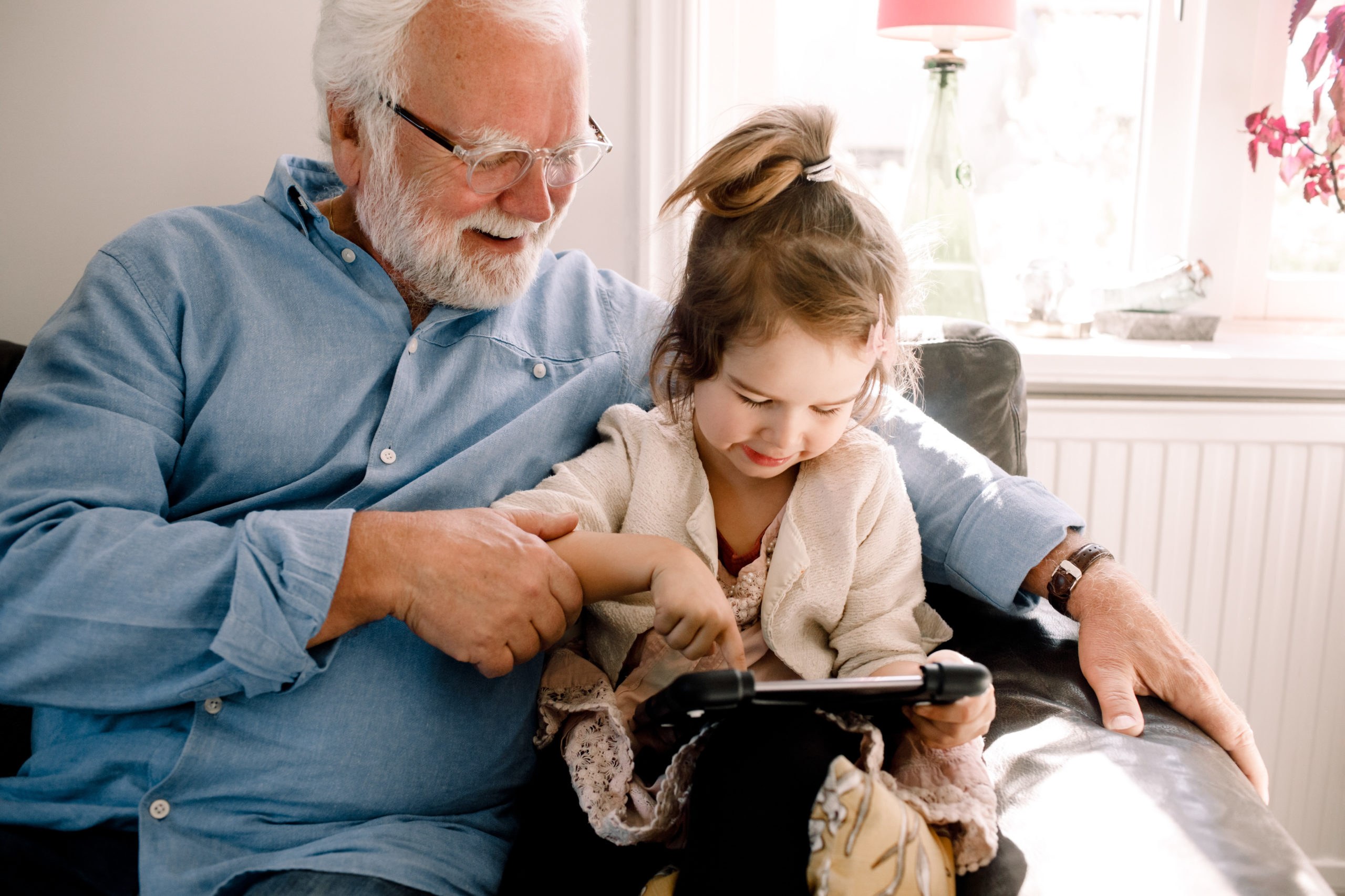Bestefar sitter med et barnebarn i armkroken og de ser på en Ipad sammen
