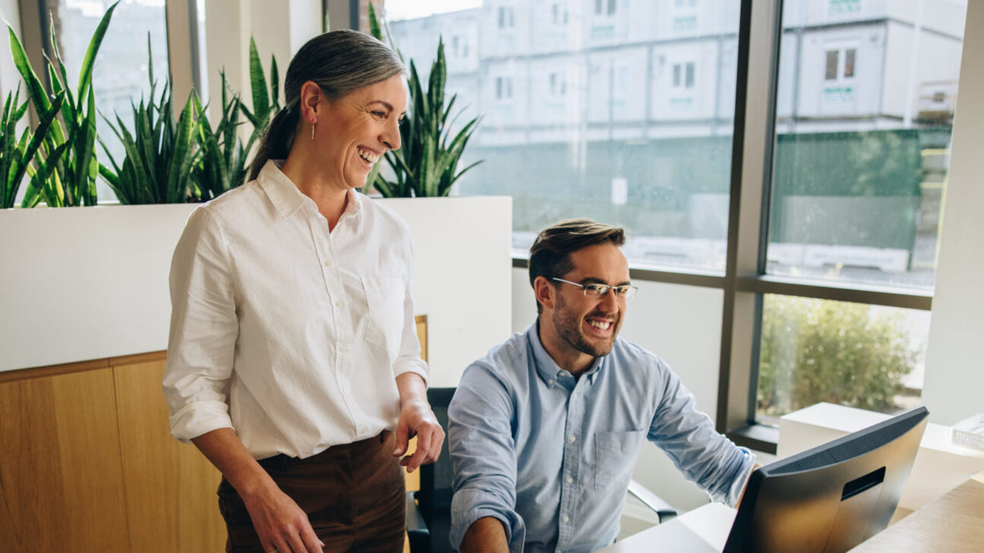 Eldre kvinner ser på PC til en yngre kollega, de ler og har det hyggelig sammen